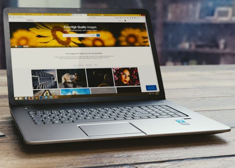 Laptop with open webpage on wooden desk, accompanied by tablet and pen, representing digital work setup.